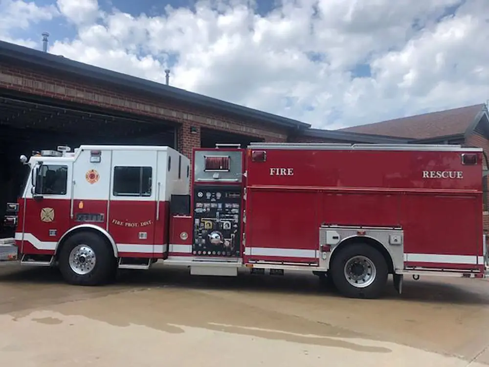 A red fire rescue truck parked outside a fire station on a sunny day.
