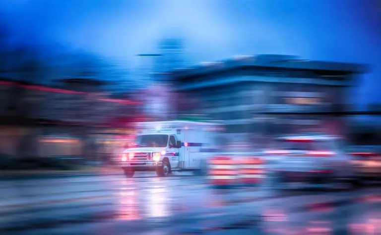 A speeding ambulance on an urgent mission, its lights a blur of motion against the evening cityscape.