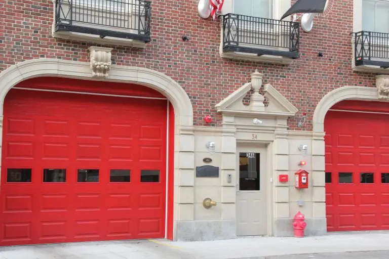 Red garage doors of a fire station with architectural detail, featuring ornate windows and a red fire hydrant on the sidewalk.
